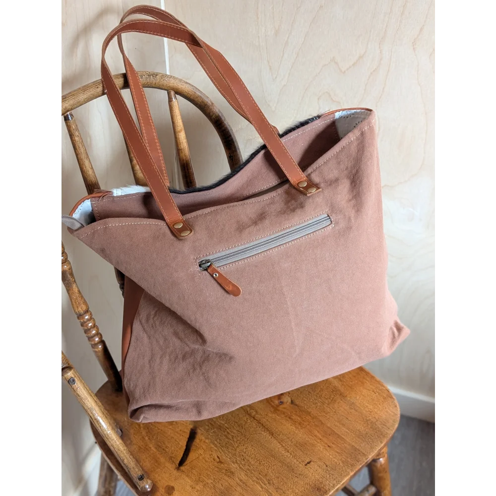 A soft dusty rose oakley specks canvas spacious bag with tan real cowhide leather handles and a matching zipper pull