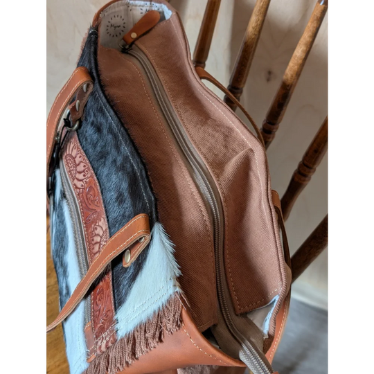 Tan and black oakley bag made of real cowhide with brown leather accents, decorative fringes, and embossed floral patterns