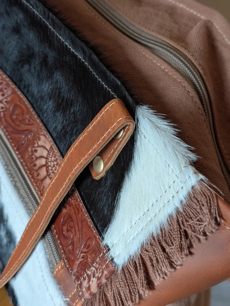 Brown leather strap with embossed floral patterns and brass buckle on oakley bag with real cowhide black and white accents