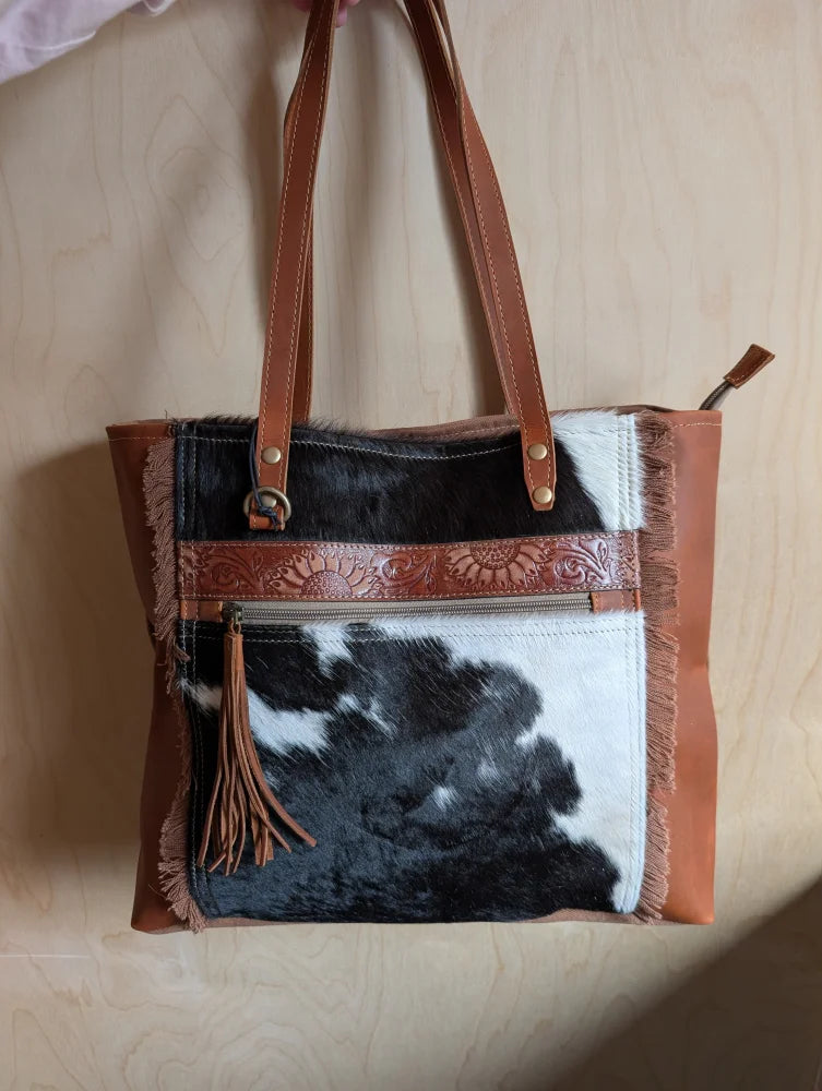 Brown and black real cowhide oakley specks canvas spacious bag with leather straps embossed floral trim and tassel accent