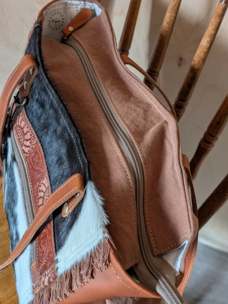 Tan and black oakley bag made of real cowhide with brown leather accents, decorative fringes, and embossed floral patterns