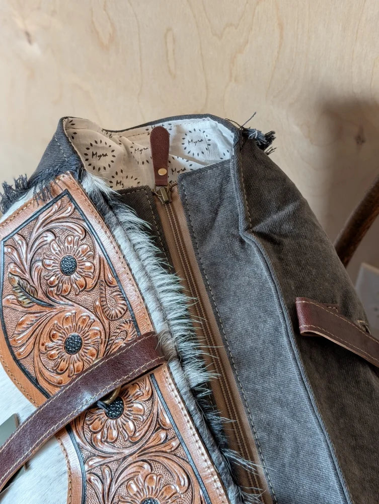 The sunflower weekender bag is a rustic brown cartwright hand-tooled bag with intricate floral tooling and hair-on hide trim