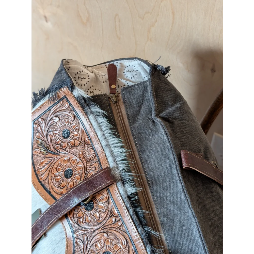 The sunflower weekender bag is a rustic brown cartwright hand-tooled bag with intricate floral tooling and hair-on hide trim