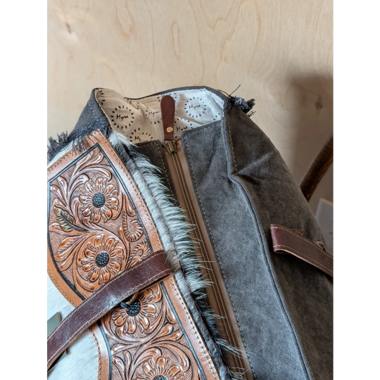 The sunflower weekender bag is a rustic brown cartwright hand-tooled bag with intricate floral tooling and hair-on hide trim