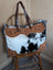 The sunflower weekender bag features a rustic cowhide hair-on hide design with tan leather embroidery and dark handles with zippered pocket