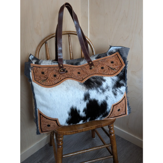 The sunflower weekender bag features a rustic cowhide hair-on hide design with tan leather embroidery and dark handles with zippered pocket