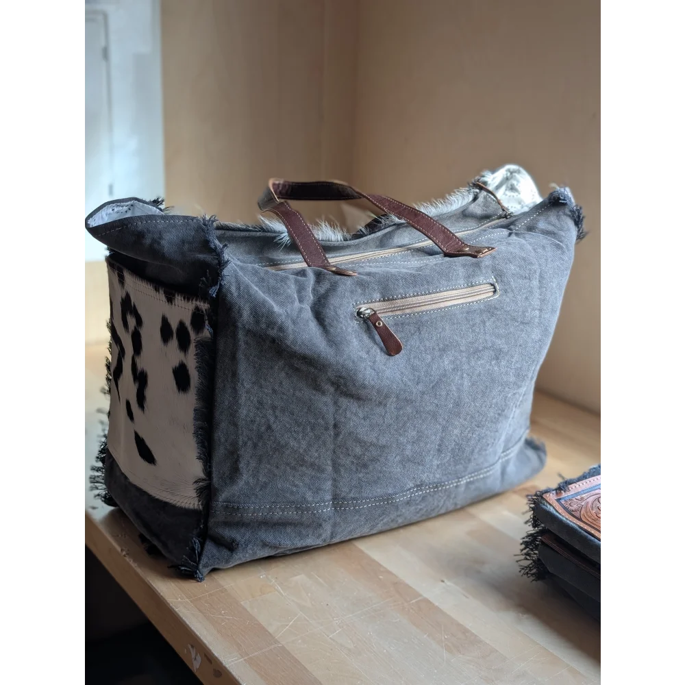 #4 the sunflower weekender bag is a gray canvas cartwright hand-tooled bag with brown leather handles and hair-on hide patch
