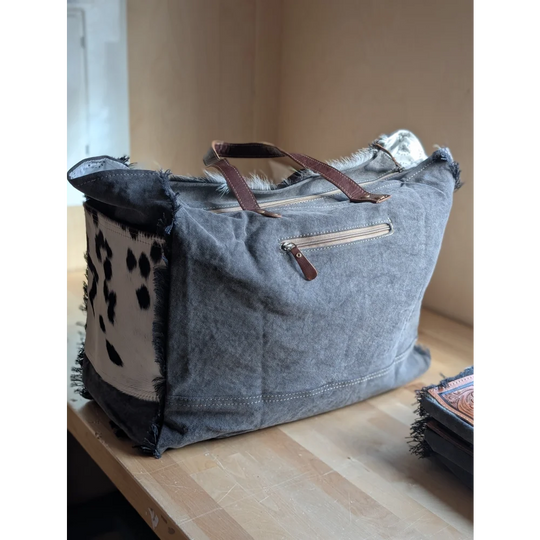 #4 the sunflower weekender bag is a gray canvas cartwright hand-tooled bag with brown leather handles and hair-on hide patch