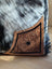 Brown leather cartwright hand-tooled bag with intricate floral design and black border on black-and-white hair-on hide background