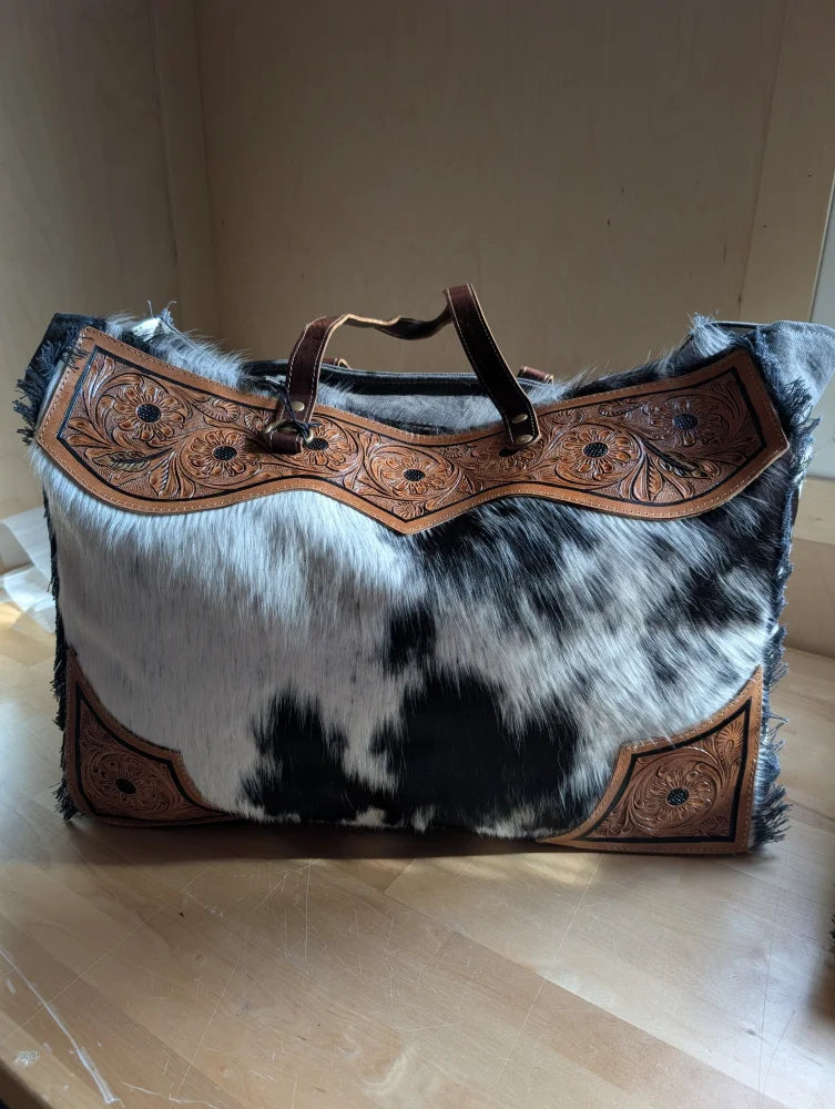 The sunflower weekender bag is a black and white hair-on hide duffle with tan leather trim and a zippered pocket