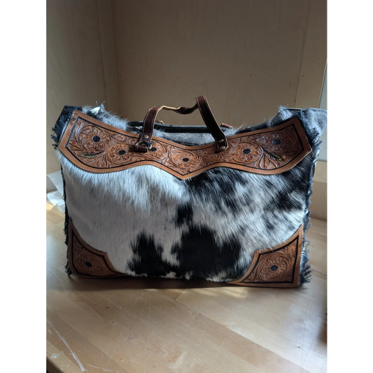 The sunflower weekender bag is a black and white hair-on hide duffle with tan leather trim and a zippered pocket