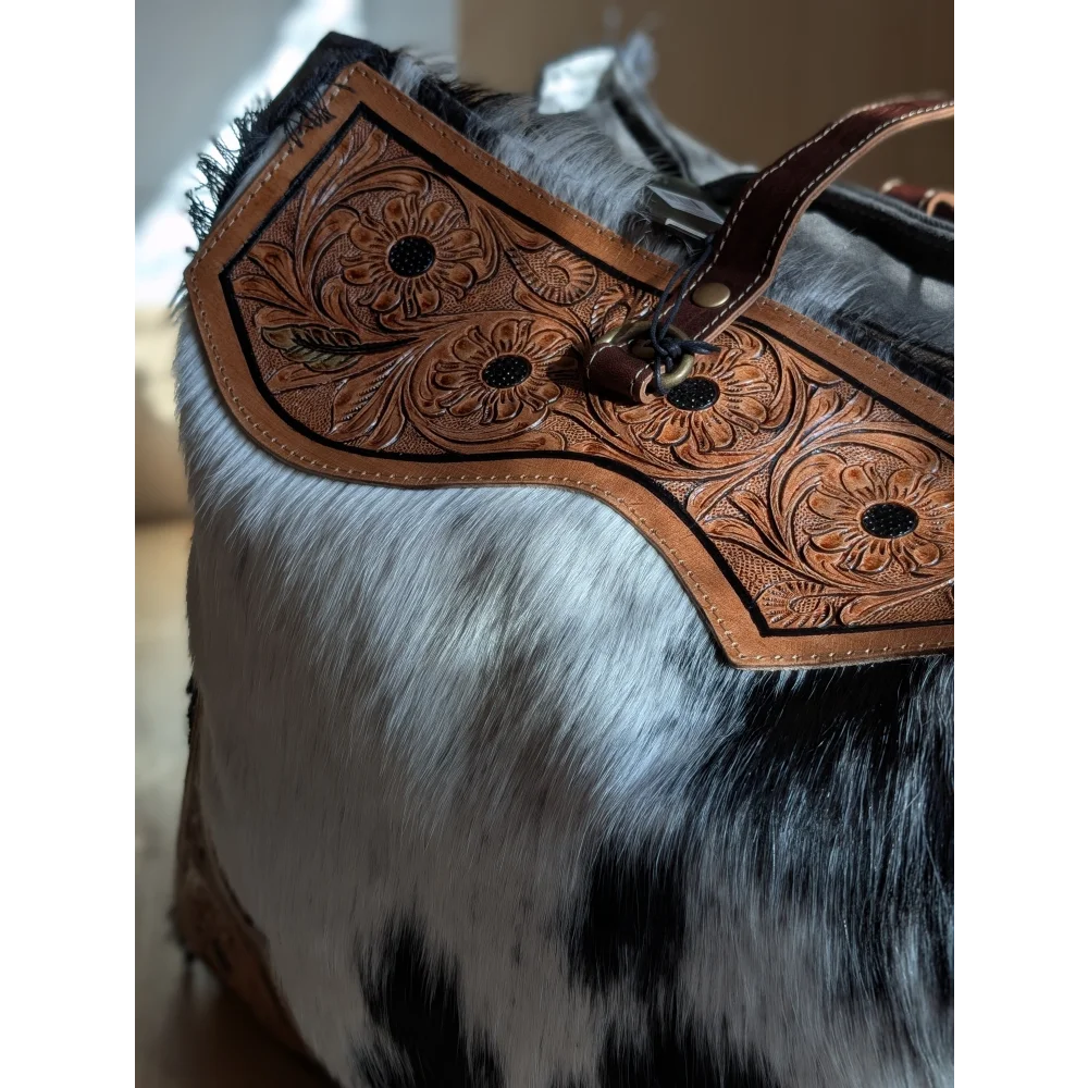 Brown leather cartwright hand-tooled bag with floral tooling, hair-on hide, sturdy strap, and metal hardware zippered pocket