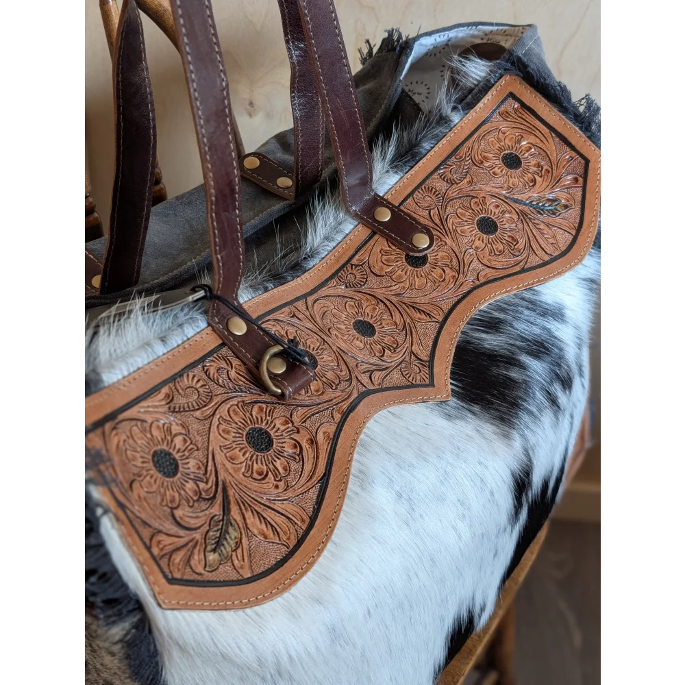 A tan cartwright hand-tooled weekender bag with floral design, dark brown straps, and a zippered pocket detail
