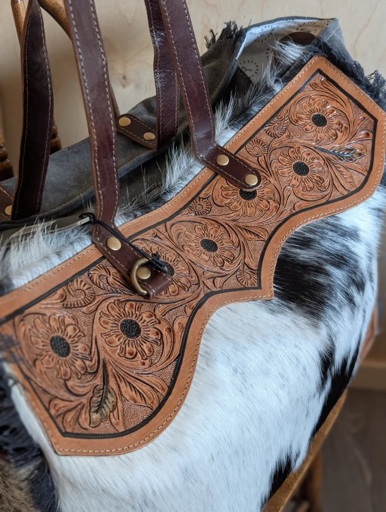 A tan cartwright hand-tooled weekender bag with floral design, dark brown straps, and a zippered pocket detail
