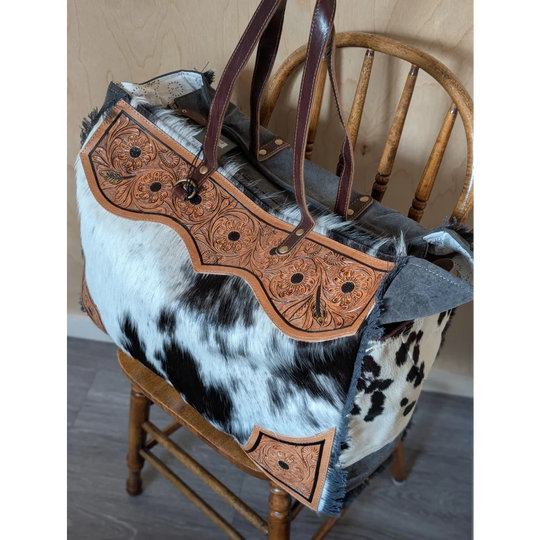 The sunflower weekender bag is a rustic hair-on hide cartwright hand-tooled bag with tan floral patterns and dark brown straps