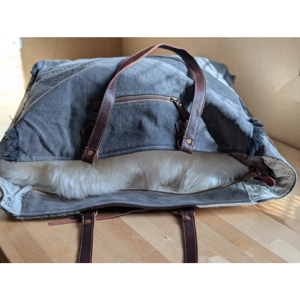 Denim tote bag with brown leather straps and white faux fur lining featuring a zippered pocket for easy storage