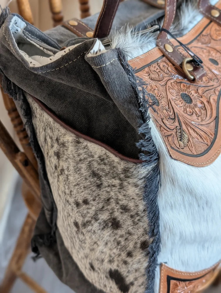 The sunflower weekender bag is a cartwright hand-tooled hair-on hide tote with floral accents white fur trim and a zippered pocket