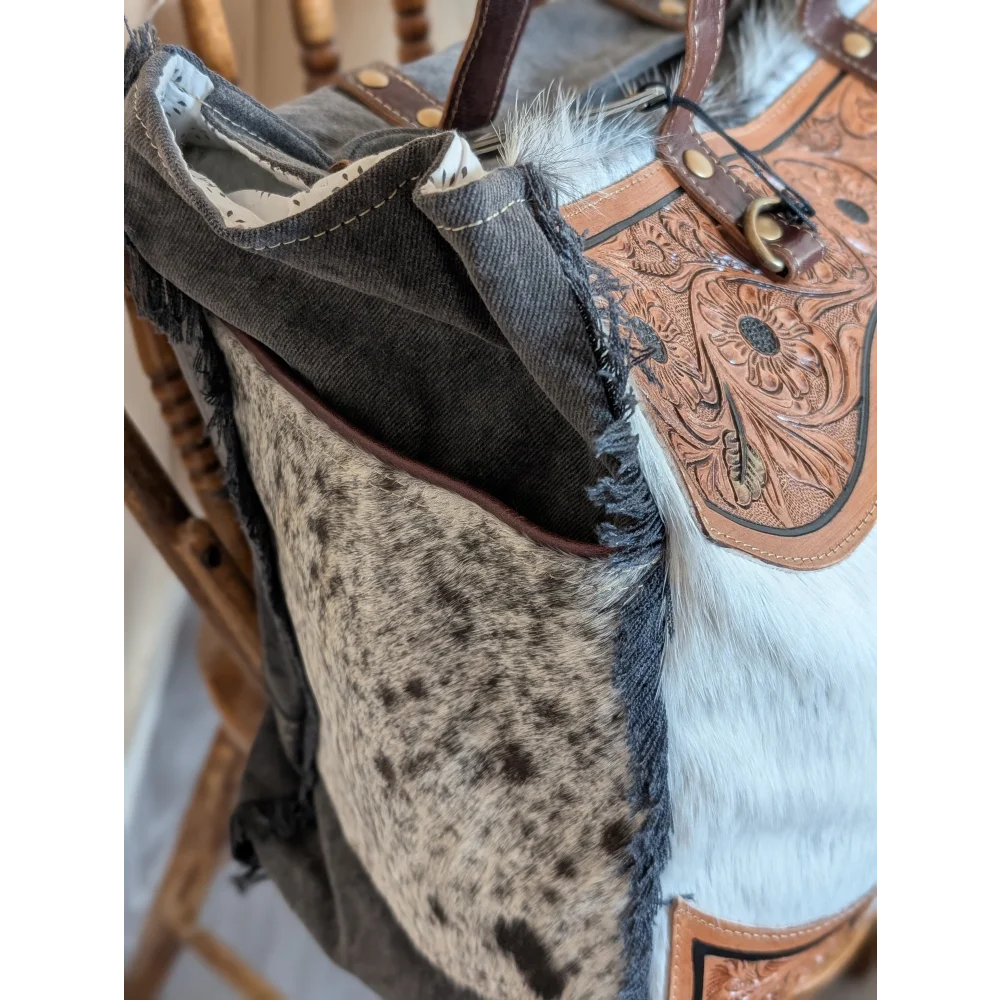 The sunflower weekender bag is a cartwright hand-tooled hair-on hide tote with floral accents white fur trim and a zippered pocket