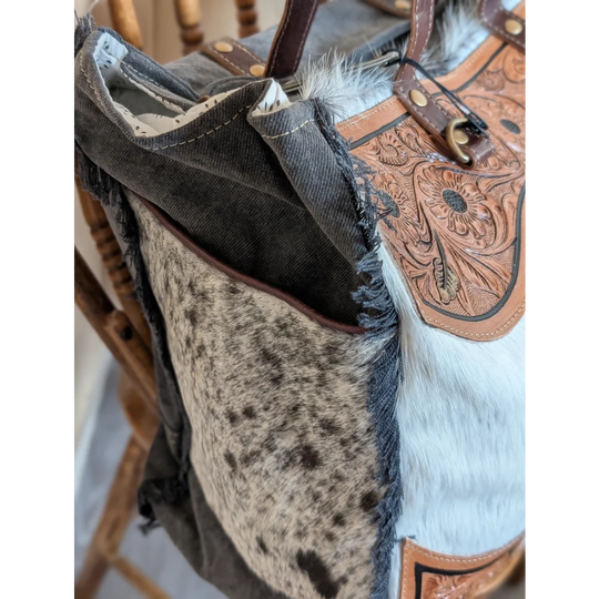 The sunflower weekender bag is a cartwright hand-tooled hair-on hide tote with floral accents white fur trim and a zippered pocket
