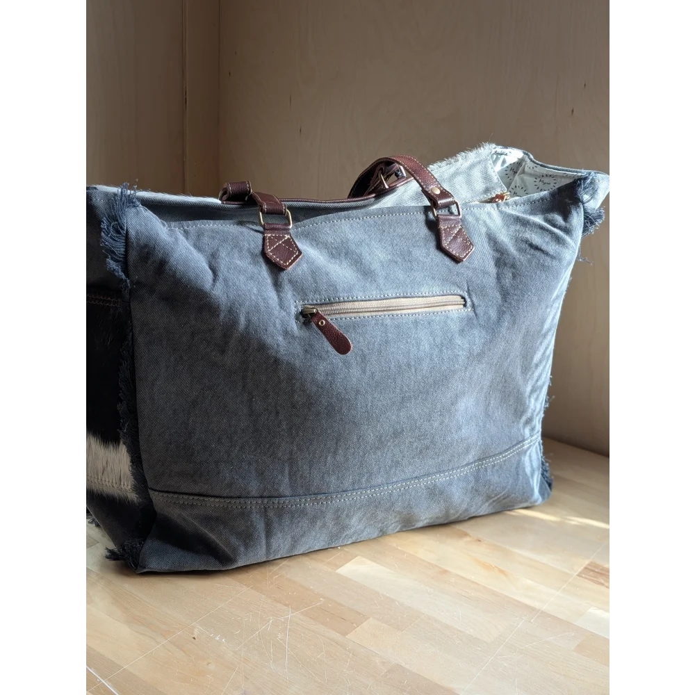 A denim sunflower weekender bag with frayed edges, brown leather handles, zipper pulls, and zippered pocket details