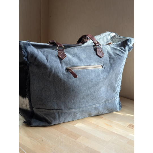 A denim sunflower weekender bag with frayed edges, brown leather handles, zipper pulls, and zippered pocket details