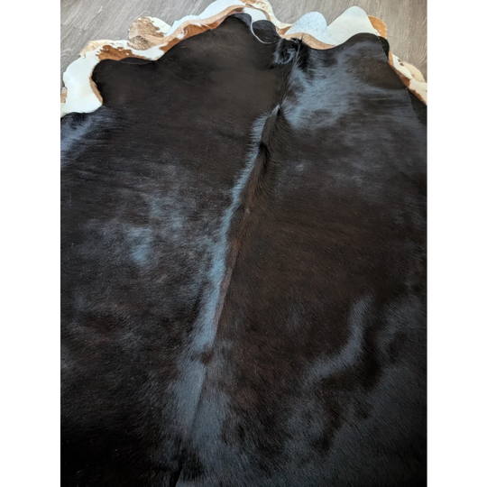 Large cowhide rug 78 x 69 inches with black base and natural irregular border featuring white and tan patches