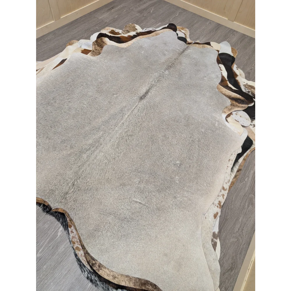 A large lovely cowhide rug measuring 77.5 by 66 inches with gray black and white natural fur patches and irregular edges