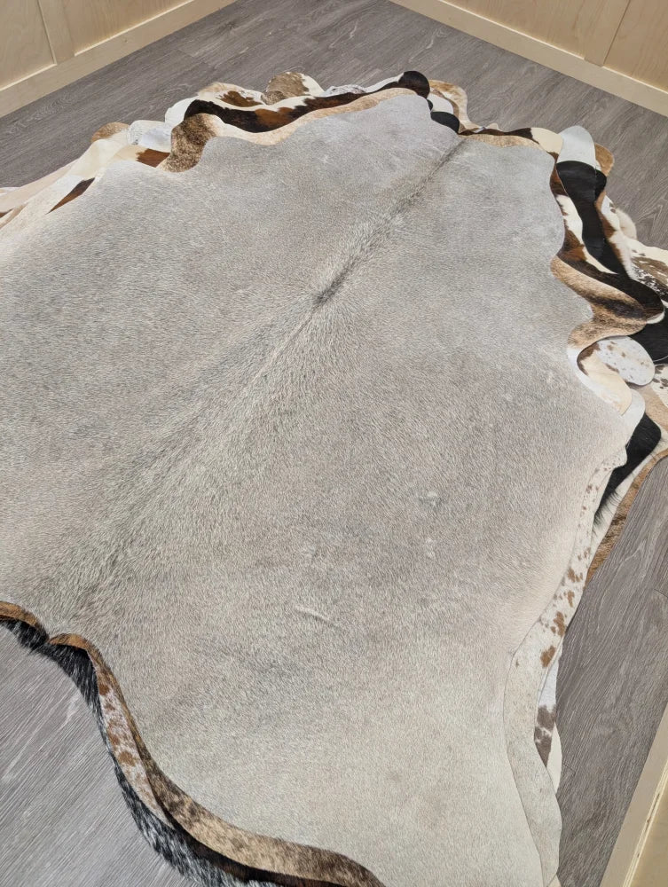 A large lovely cowhide rug measuring 77.5 by 66 inches with gray black and white natural fur patches and irregular edges