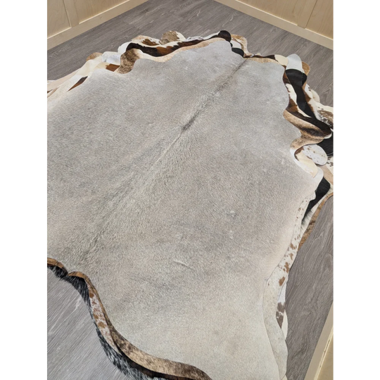 A large lovely cowhide rug measuring 77.5 by 66 inches with gray black and white natural fur patches and irregular edges