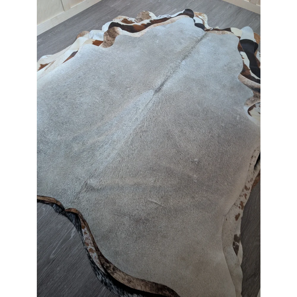 A lovely large cowhide rug in light gray with natural edges and brown and black patches measuring 77.5 x 66 inches