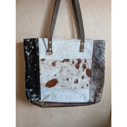 A stylish cowhide tote bag with patchwork white brown and black spots dark brown leather straps real cowhide design