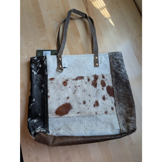 A stylish cowhide tote bag with white and brown patchwork and black leather sides from real cowhide rugs collection