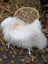 A plush natural white icelandic sheepskin long wool throw draped over a woven wicker chair with white legs