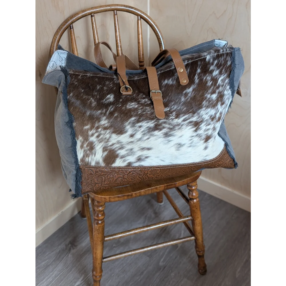 Brown and white cowhide matty affair canvas shoulder bag with denim accents tan leather straps and buckle closures by angus oliver