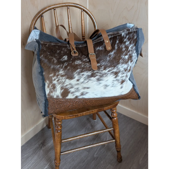 Brown and white cowhide matty affair canvas shoulder bag with denim accents tan leather straps and buckle closures by angus oliver
