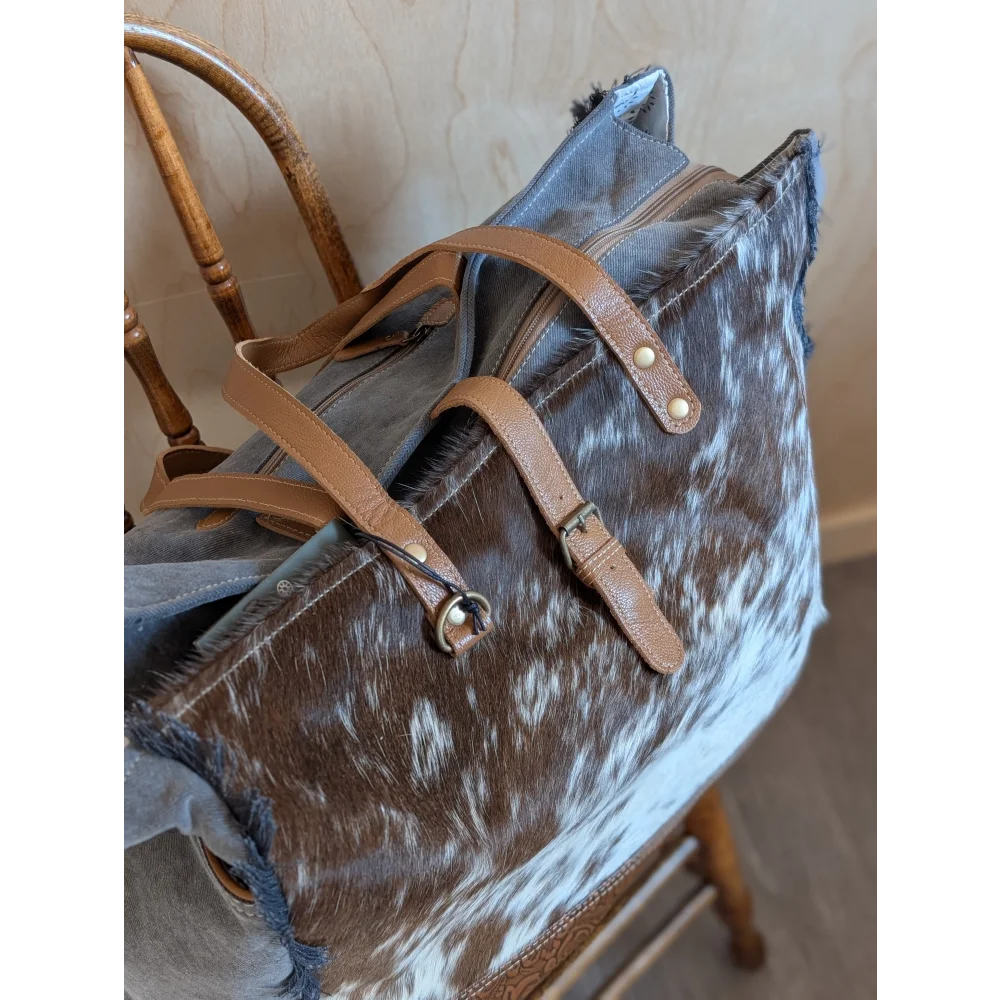Brown and white cowhide duffle bag with tan leather straps and metal hardware from angus oliver matty affair canvas line