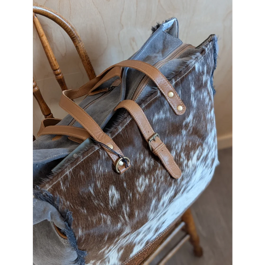 Brown and white cowhide duffle bag with tan leather straps and metal hardware from angus oliver matty affair canvas line
