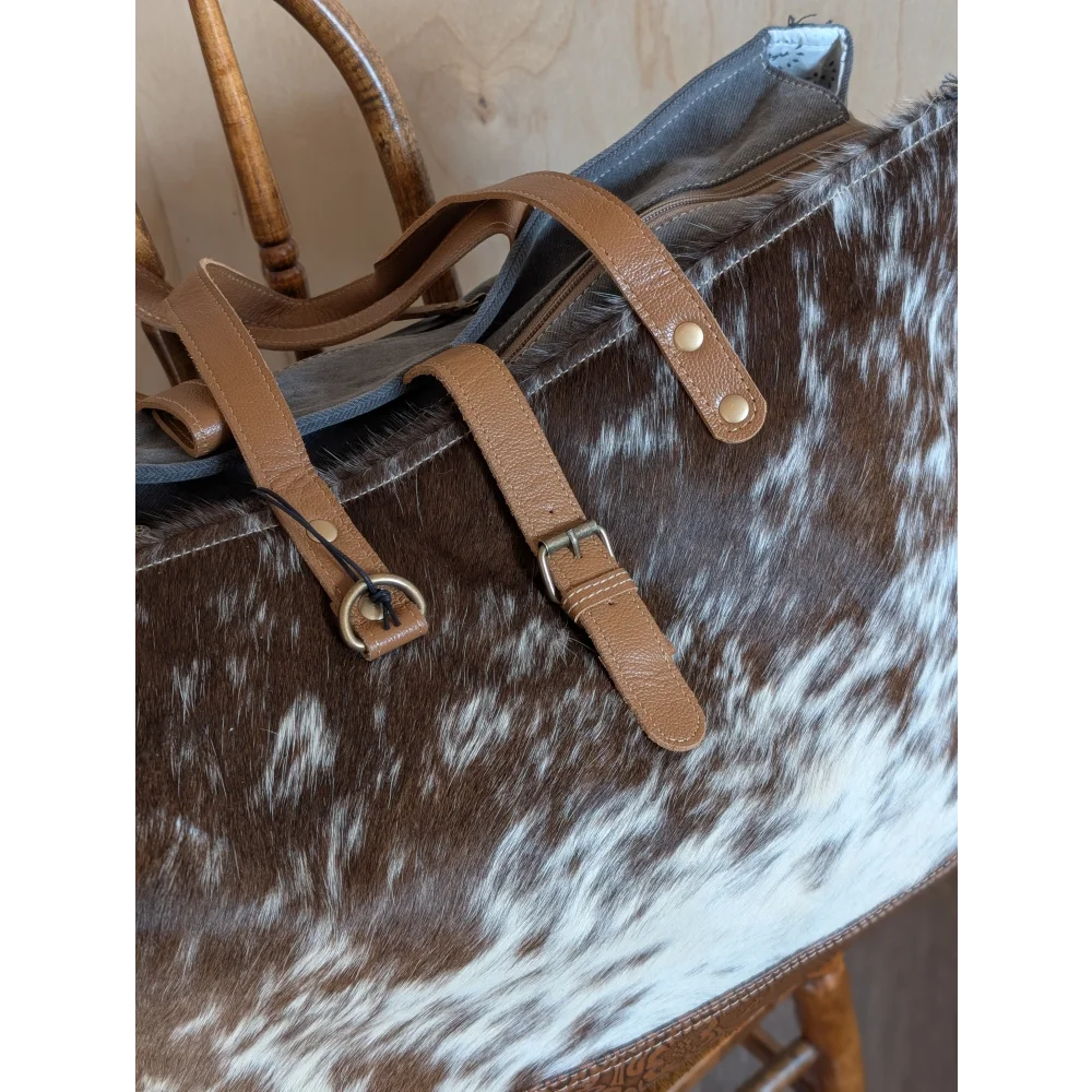 Brown and white cowhide duffle bag with tan leather straps and brass hardware from angus oliver matty affair canvas collection