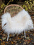 White fluffy large long wool natural white icelandic sheepskin throw draped over a wicker chair with white metal legs