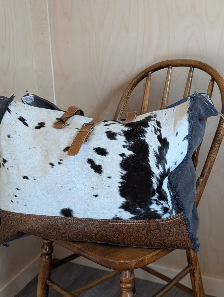 A white and black cowhide duffle bag with tan leather straps and brown embossed leather base from angus oliver affair canvas hair