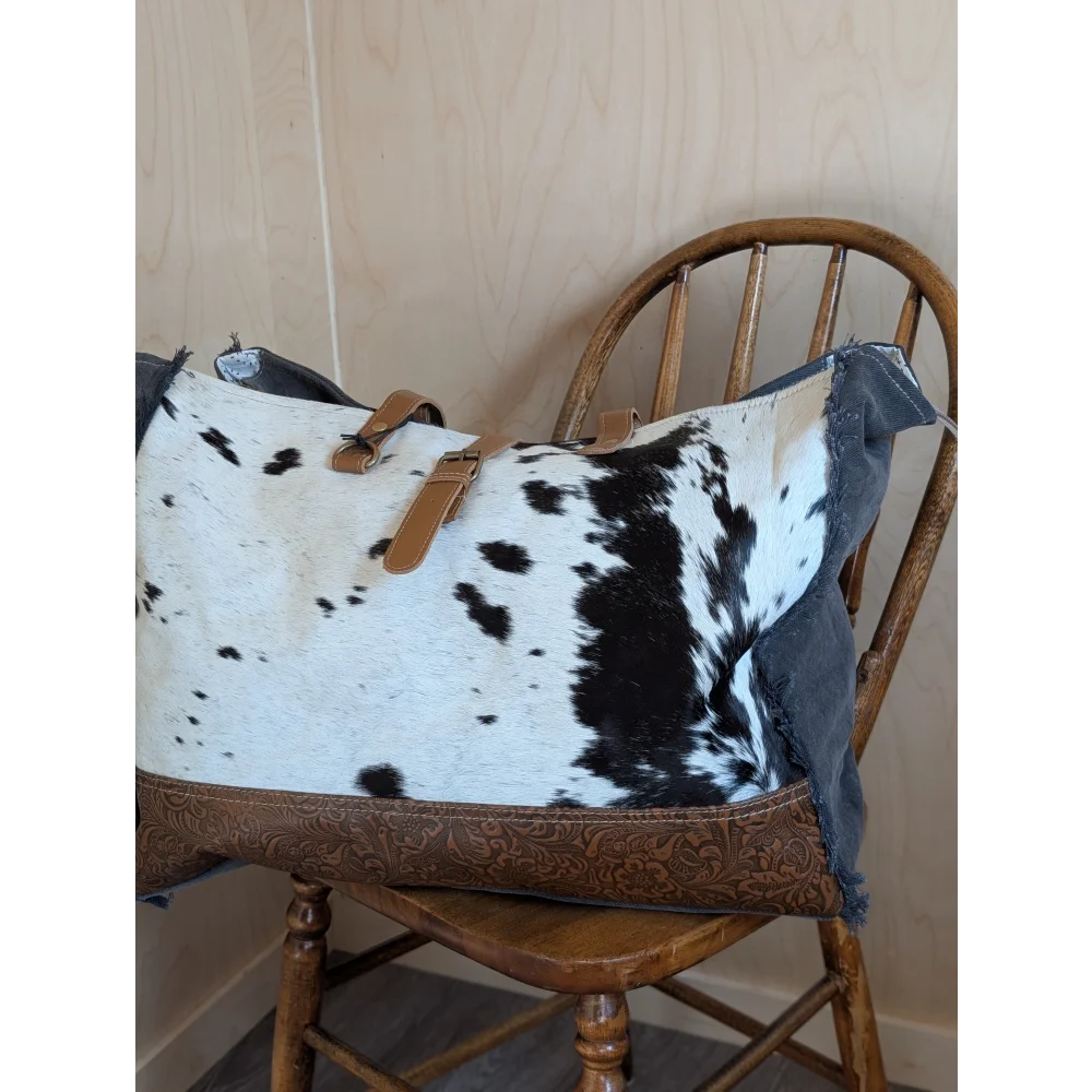 A white and black cowhide duffle bag with tan leather straps and brown embossed leather base from angus oliver affair canvas hair