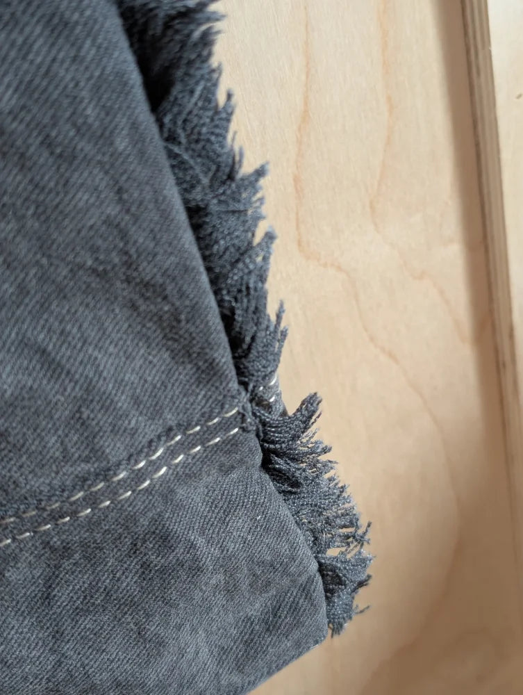 Dark gray denim fabric with frayed edges and white stitching on angus oliver matty affair canvas weekender bag