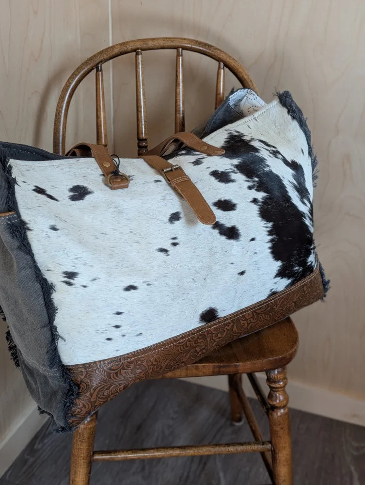 A stylish black and white cowhide duffle bag with brown leather straps and embossed trim from angus oliver matty affair canvas