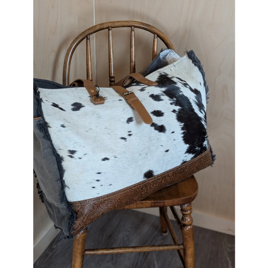A stylish black and white cowhide duffle bag with brown leather straps and embossed trim from angus oliver matty affair canvas