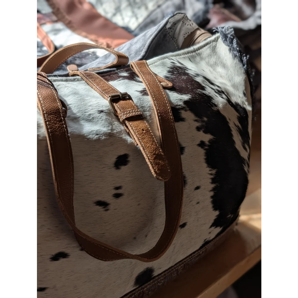 A matty affair canvas hair cowhide duffle bag with brown leather straps and black and white spotted angus oliver pattern