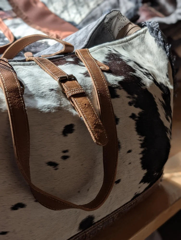A matty affair canvas hair cowhide duffle bag with brown leather straps and black and white spotted angus oliver pattern