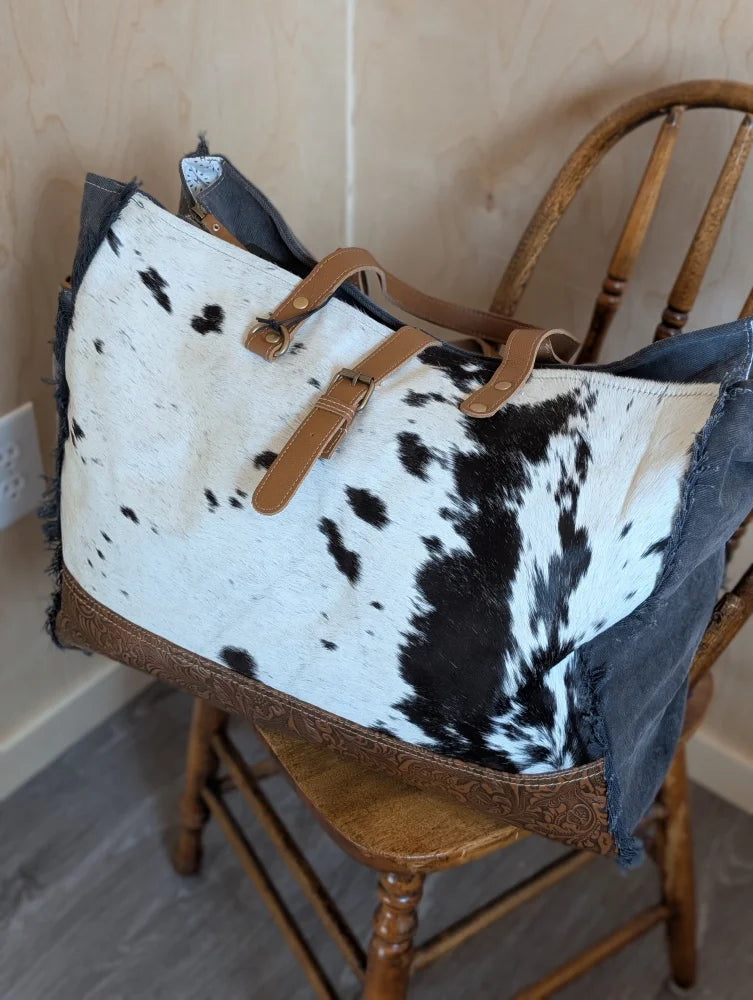 A black and white cowhide #6 matty affair canvas tote bag with tan leather straps and brown leather trim by angus oliver