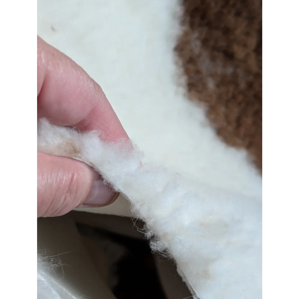 White fluffy cotton batting held between fingers from grade a- highland spotted sheepskin product