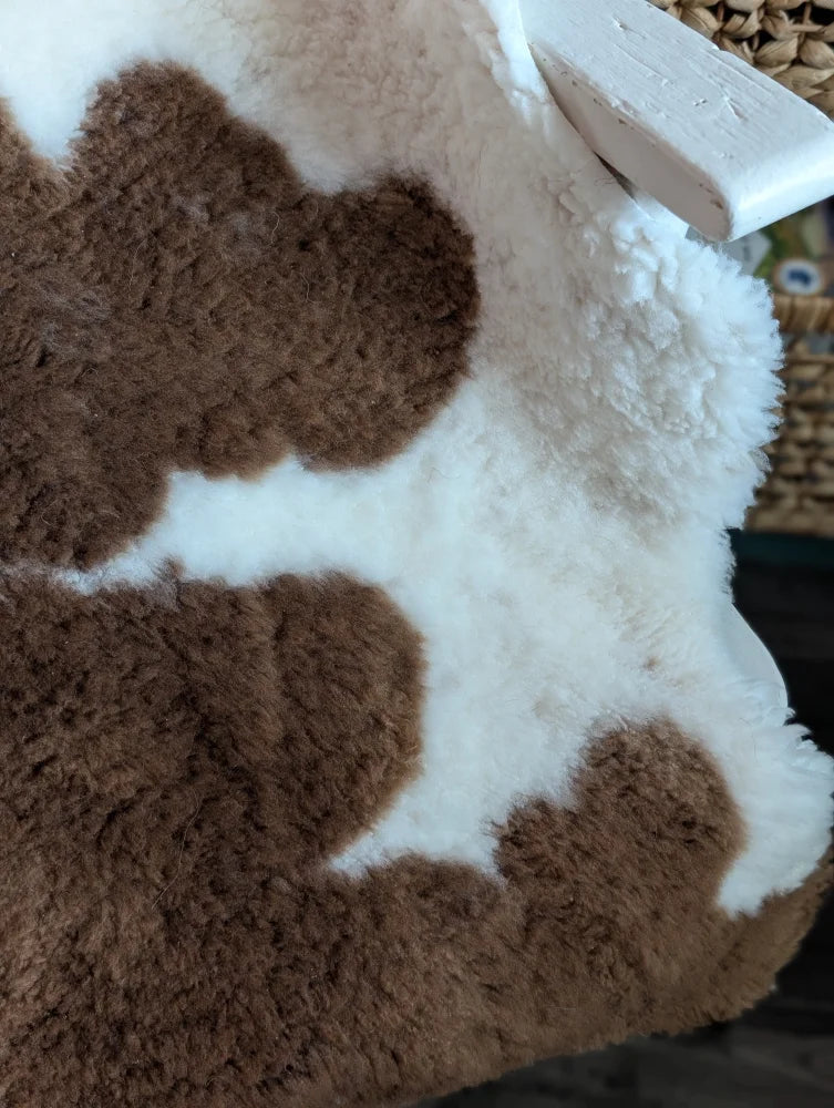 A plush brown and white cow print throw blanket made from grade a- highland spotted sheepskins with a fluffy texture