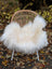 A cozy natural white icelandic sheepskin with long wool draped over a woven rattan chair with white legs
